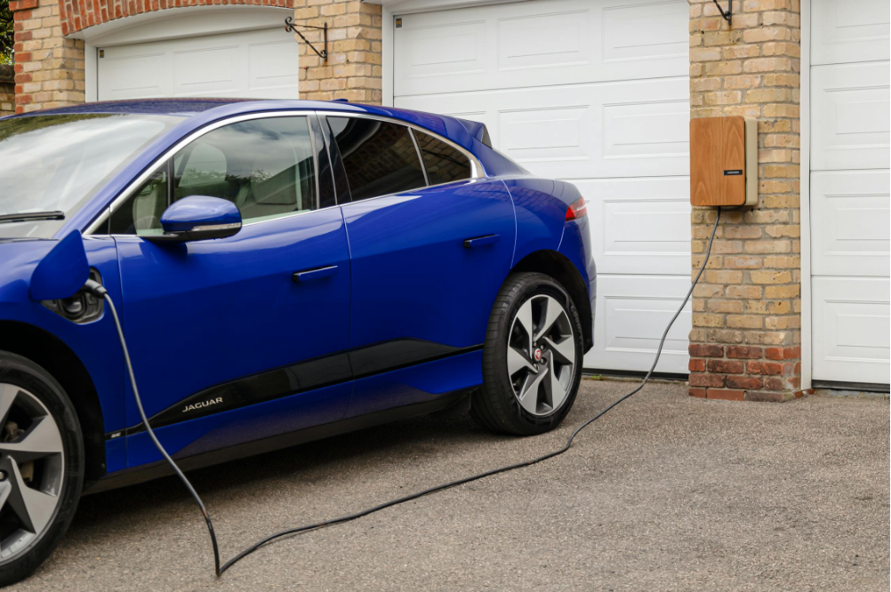 Blue Jaguar I-PACE electric SUV charging at residential home with wall-mounted EV charger in San Antonio